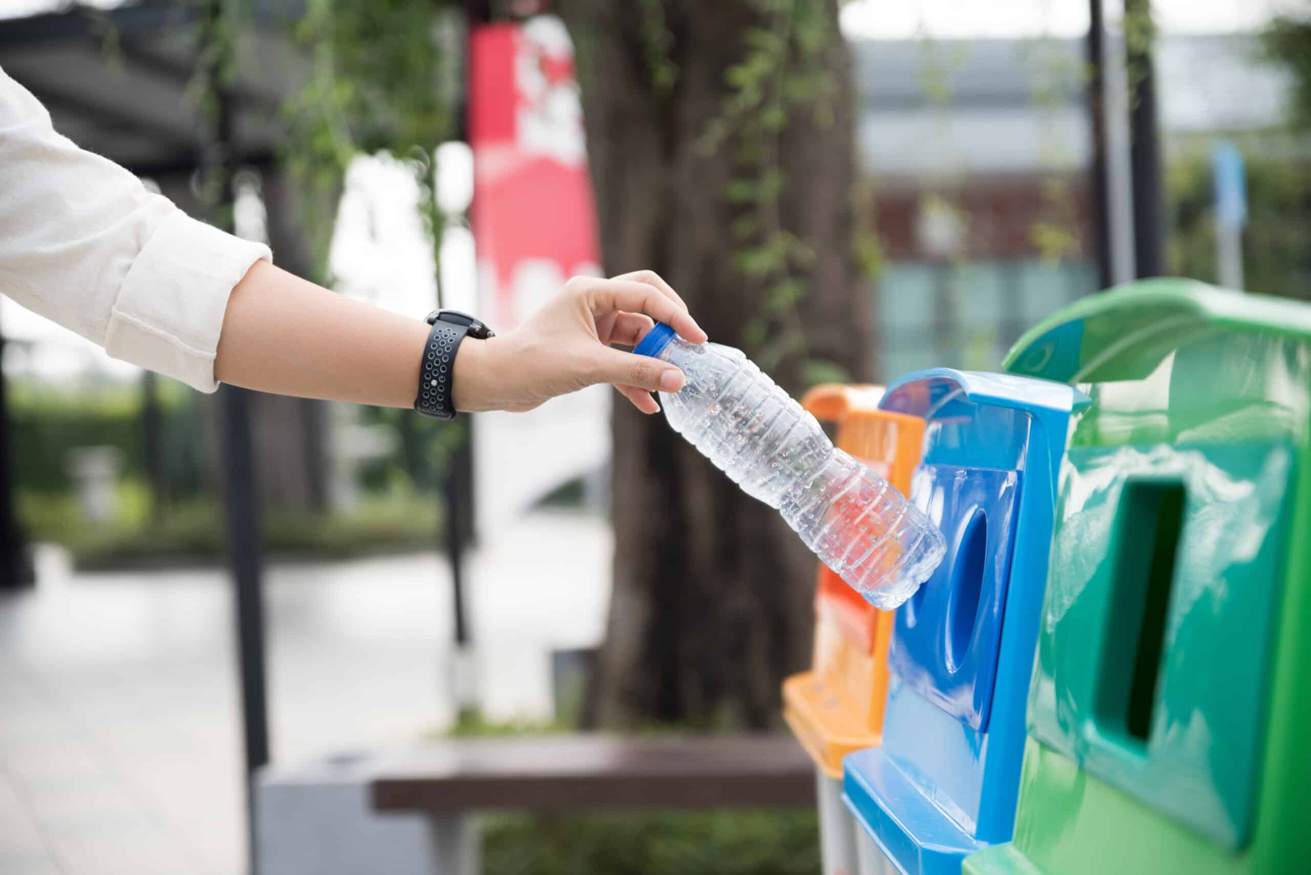 Closeup portrait woman hand throwing empty plastic water bottle in recycling bin.